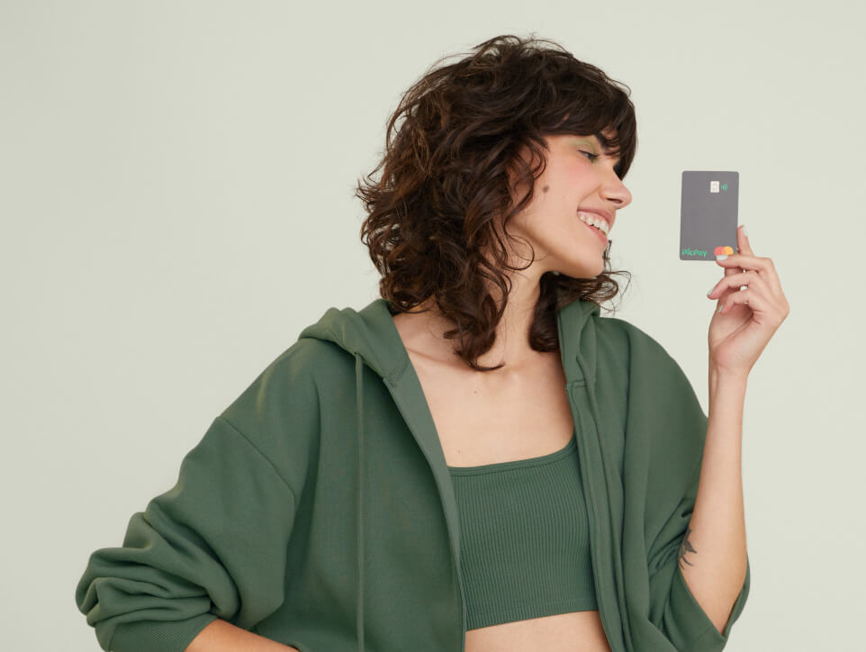 Para todos verem: uma mulher usando uma roupa verde segura o cartão picpay em suas mãos. Imagem retirada do site oficial PicPay.